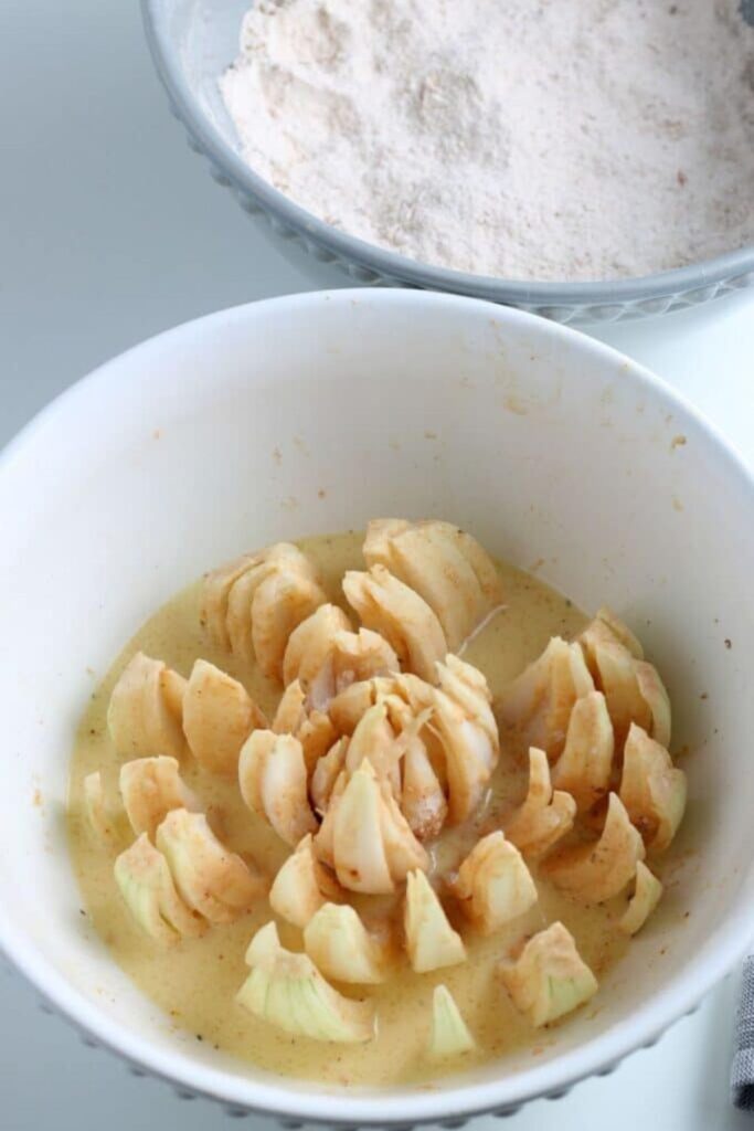 a white bowl with a breaded blooming onion on the table with flour to the top of the table in a plate