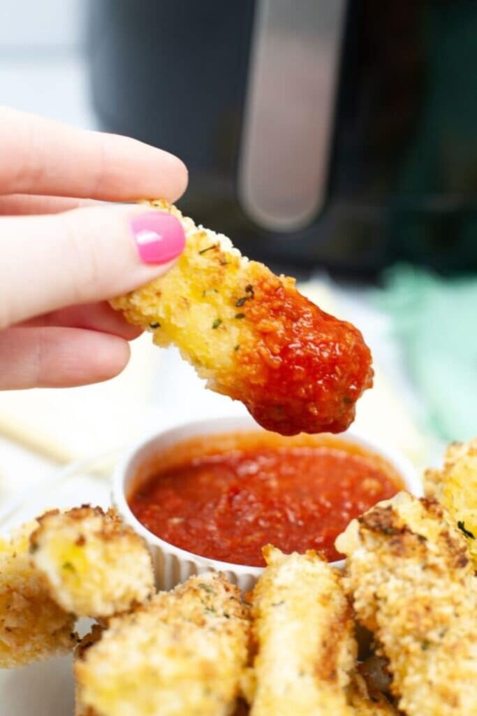 moozzarella sticks being dipped in marinara sauce
