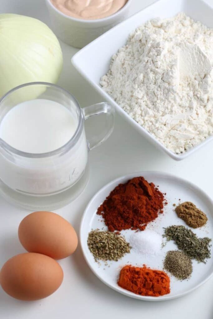 all the ingredients to make air fryer onion blossom on table on plates or in containers to show each ingredient