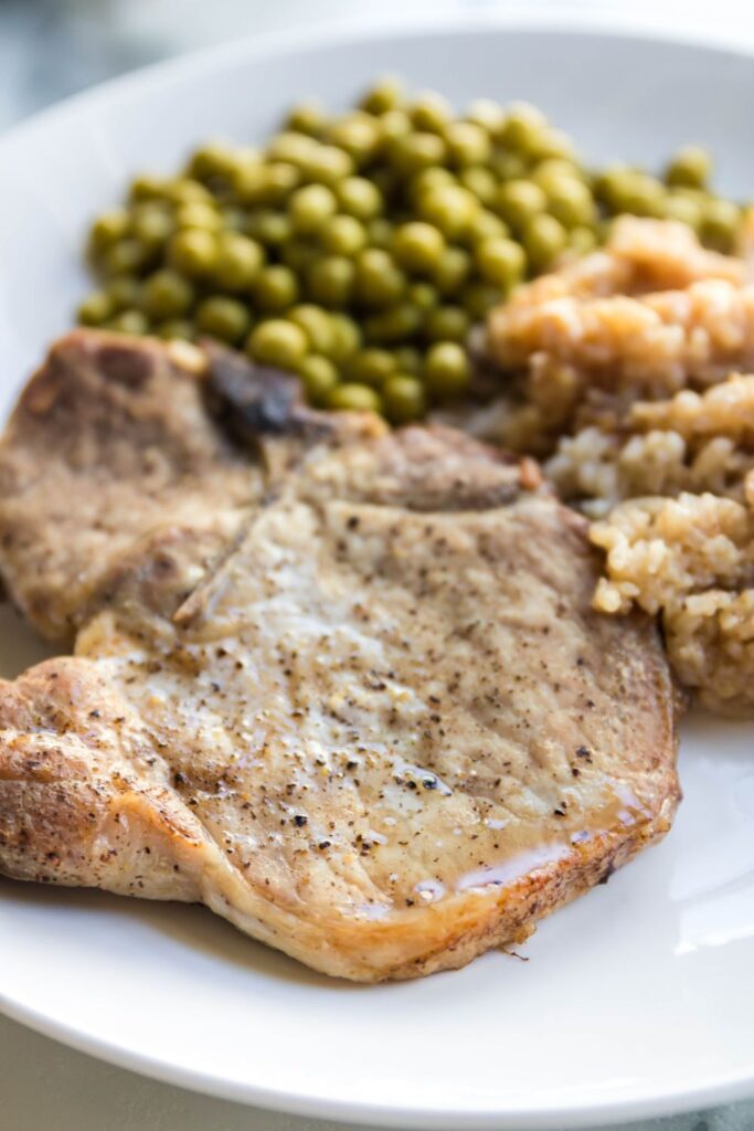 pork chops, rice and peas on a white plate