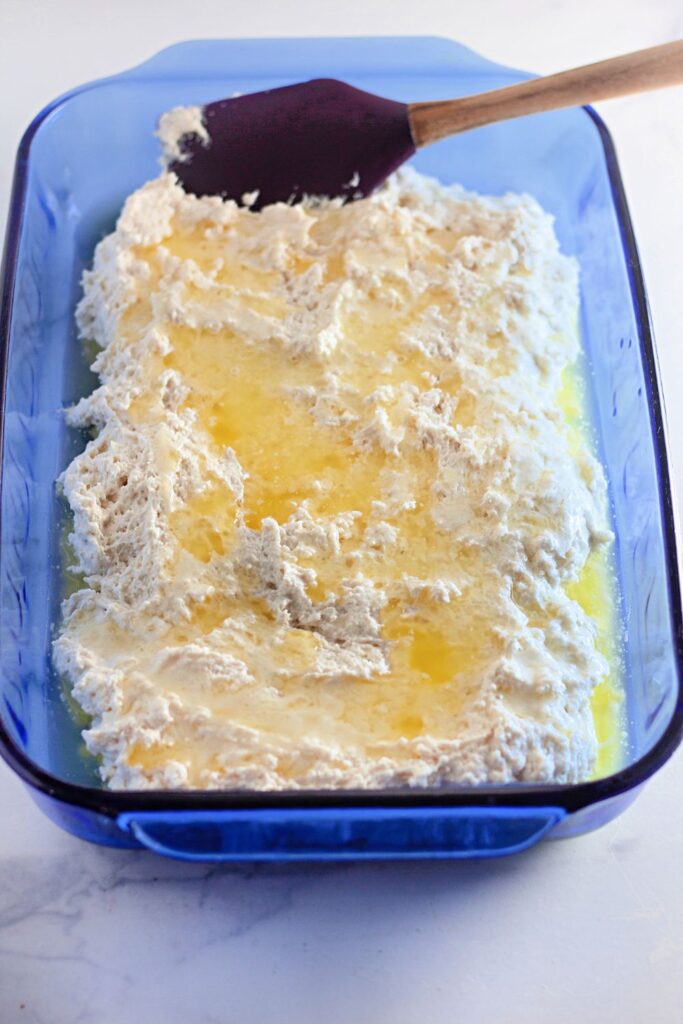 butter poured over biscuit dough in a 9x13 pan