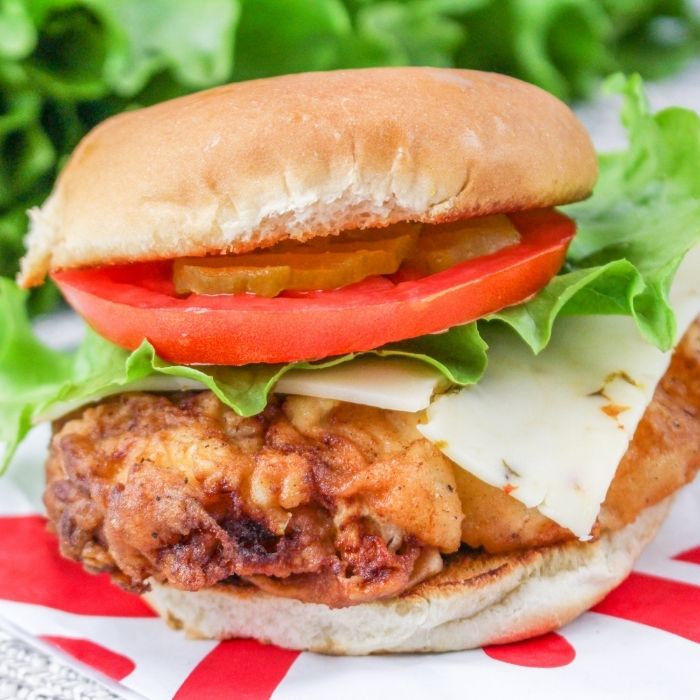 spicy chicken sandwich on table with lettuce, tomatoes, and cheese