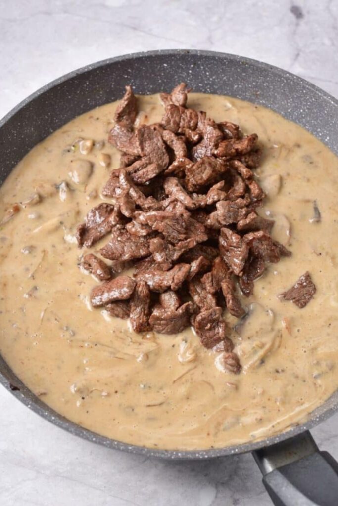 creamy sauce in pan that has a bunch of cooked steak on top