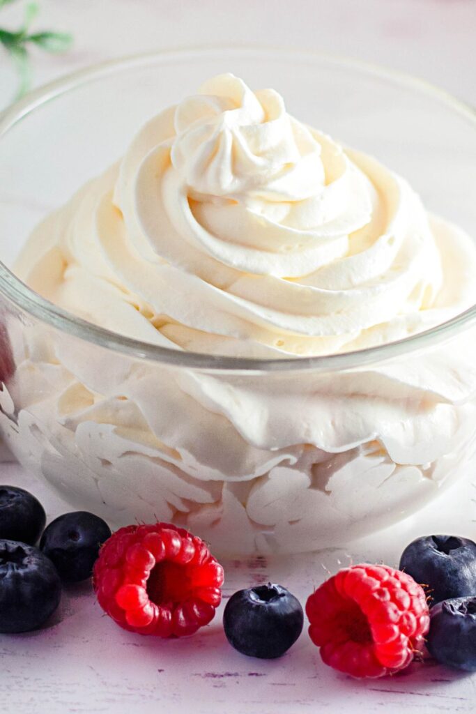fluffy whipped topping piped into a glass bowl with berries around it