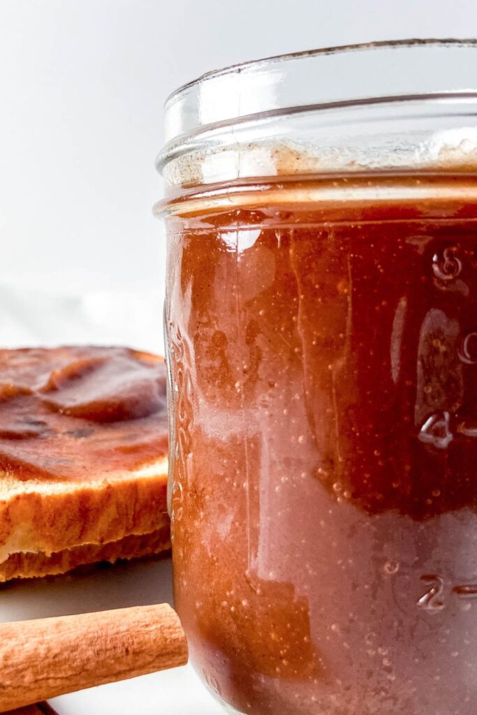 mason jar with apple butter in it and toast in the background on a plate