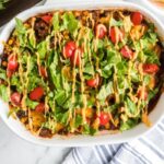 Layered Beef Enchilada Casserole in a white pan with a towel in the front