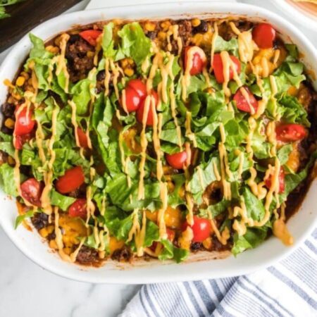 Layered Beef Enchilada Casserole in a white pan with a towel in the front