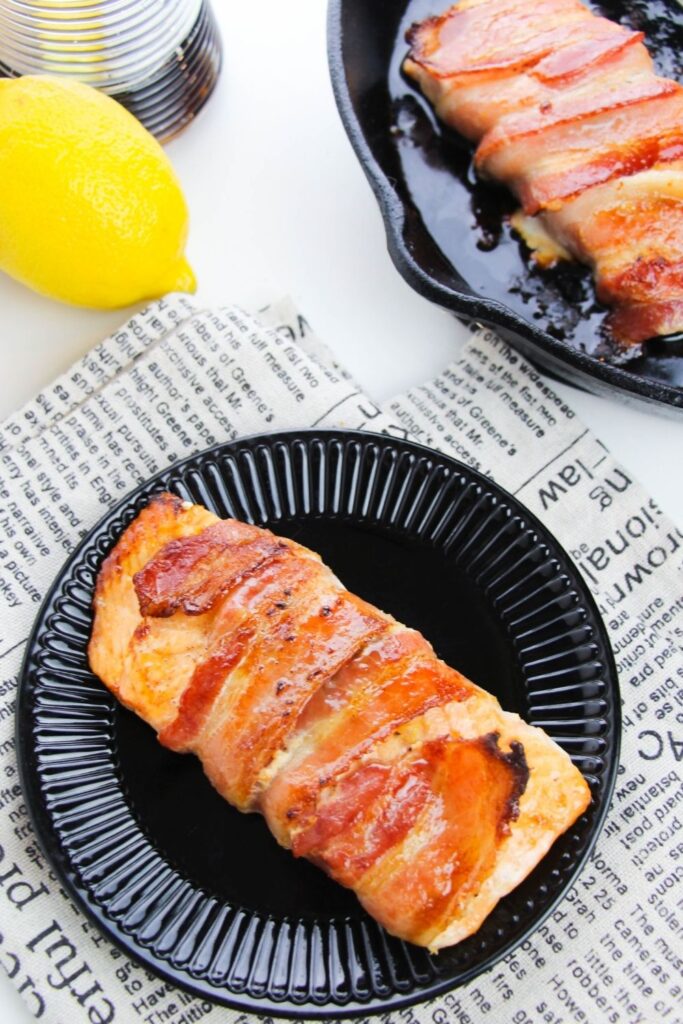 maple bacon salmon on black plate with lemon behind it