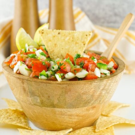 wooden bowl with pico de gallo in it with a tortilla chip in the bowl and scattered around the bowl