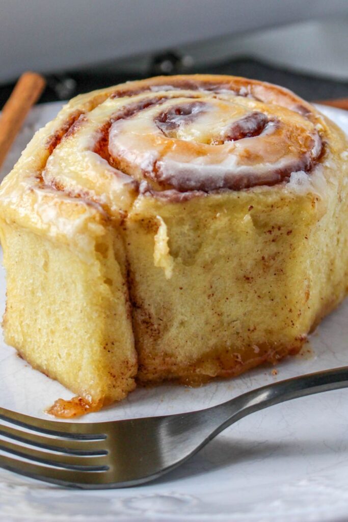 cinnamon roll on plate with a fork in front of plate
